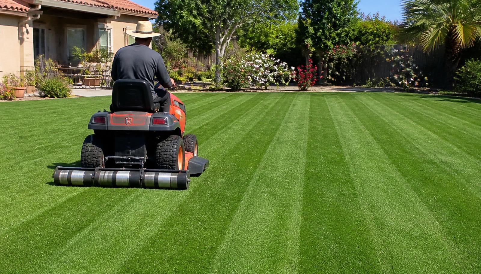 Riding mower with a rear striping roller laying down light and dark stripes on a Bermuda grass lawn